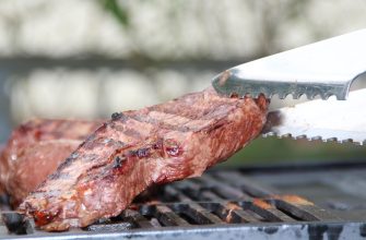 Beef steak cooking on a barbecue grill with a serrated metal tongs lifting the edge