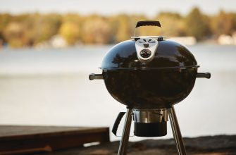 Kettle-style charcoal grill with a built-in thermometer, set up outdoors by a lake.