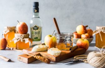 Rustic still life with apples, jars of honey, jam, a wooden board with cheese, and a spooned jar centerpiece.
