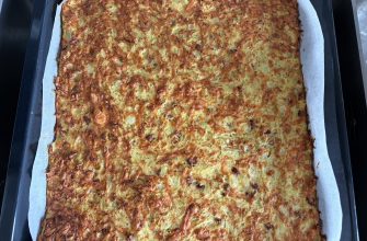 Large sheet pan of golden-brown cheesy potato bake with visible potato chunks, parchment lining on the sides.