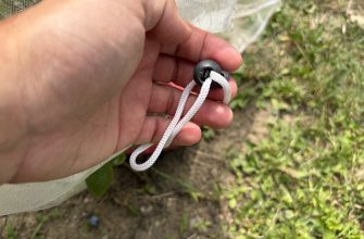 Close-up of a hand tightening a white drawstring with a black cord lock on a light fabric bag outdoors.