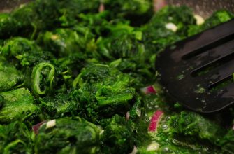 Sautéed chopped leafy greens with onions in a pan, a black spatula resting on top.