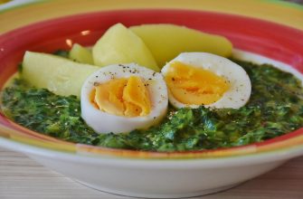 Bowl of creamy spinach soup topped with two halved soft-boiled eggs and potato chunks in a colorful bowl.