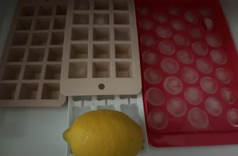 Yellow lemon resting on a white tray in front of a white square-grid mold and a pink circular-m molds tray