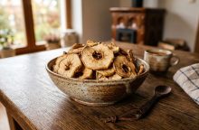 Ceramic bowl of dried apple rings on a wooden table in a cozy kitchen.